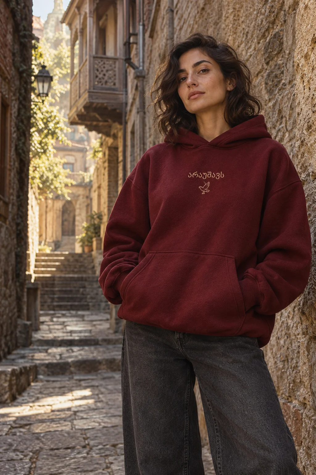 Model wearing the wine red Araushavs hoodie with small Georgian lettering in a Tbilisi lane